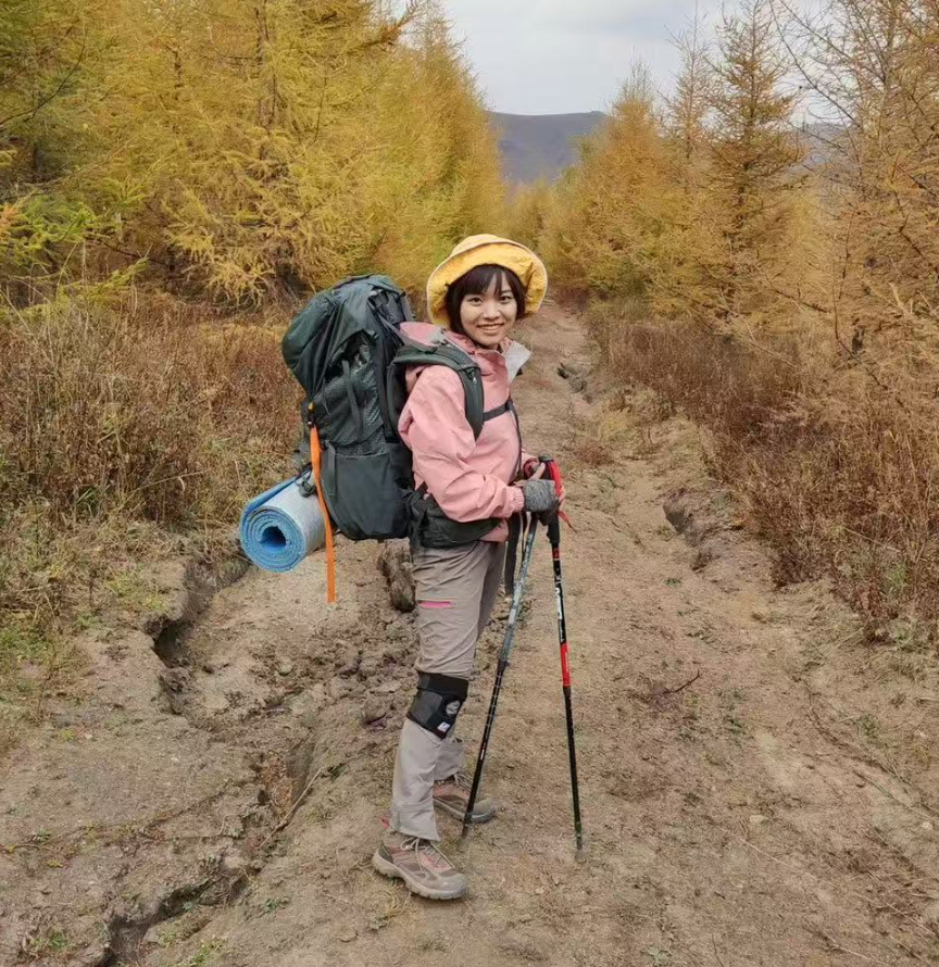 Yumei He hiking on a forest trail with a backpack and trekking poles